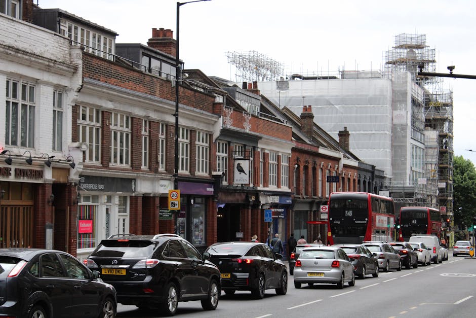 A busy street scene in Enfield with a corner building featuring a white façade and multiple large windows, housing a pub called 'The World's End.' The street is filled with pedestrians waiting at the