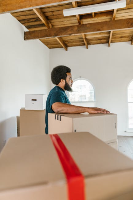 Two professional movers from Man and Van Enfield are engaged in loading a large, cushioned piece of furniture wrapped in green fabric into the open back of a white van parked on a street in Enfield. T
